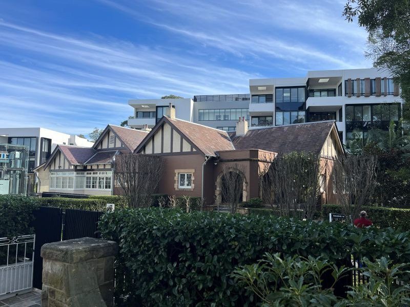 A Federation house in its garden, with a new apartment block rising directly behind it