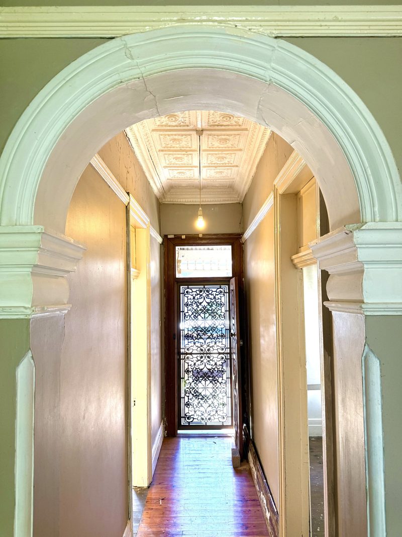 Looking through a plaster archway down a Victorian hallway to the front door, under an ornate ceiling