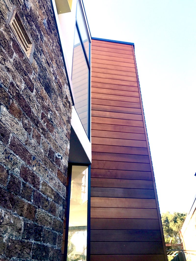 Upward view of a small modern building in Dulwich Hill with a stone brick wall and a section with horizontal siding