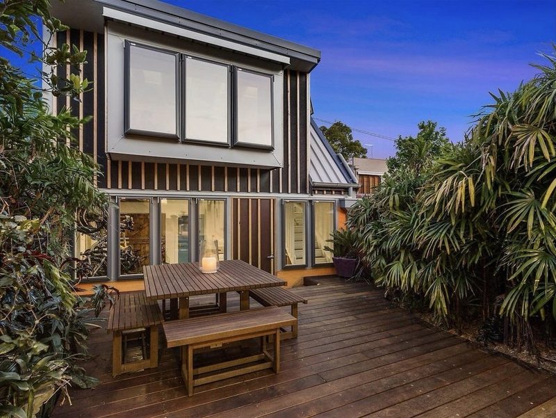 Timber-clad rear extension lit from within at twilight, opening onto a deck, Erskineville