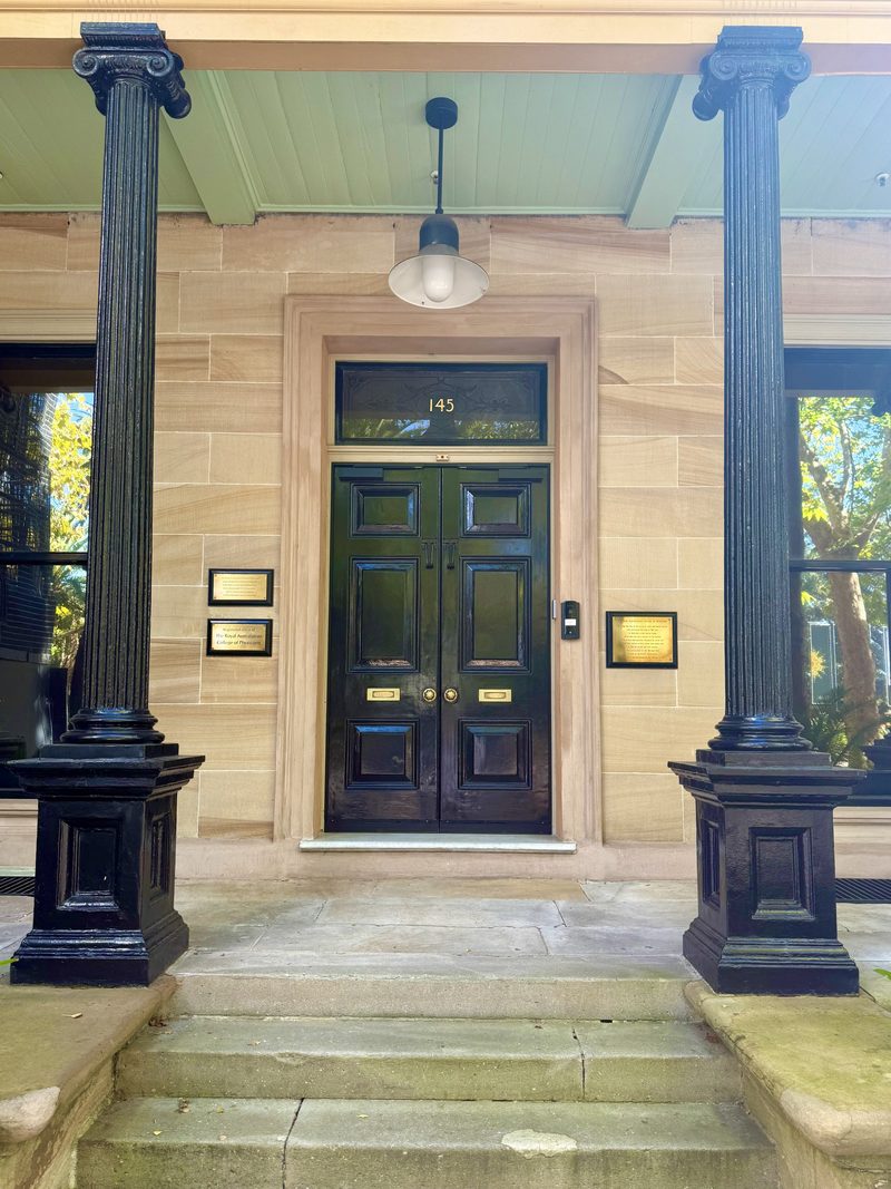 The sandstone entrance of a heritage building: black panelled double doors between two fluted columns
